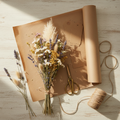 Overhead flat-lay of dried flower stems, kraft paper, and twine on a wooden table