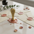 Wax seal stamp with floral crest, melted blush wax and sealed envelopes on a marble desk