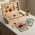 Wooden flower press open with pressed petals beside two glass frames on linen